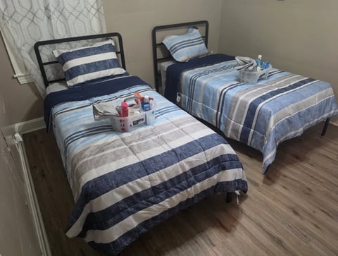 Two twin beds with blue and white striped bedding and dark metal frames in a bedroom with hardwood flooring