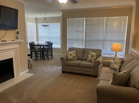 Spacious living room with beige furniture, fireplace, and oceanview through sliding glass doors with shutters.