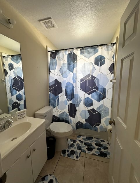Modern bathroom with white vanity, toilet, and geometric patterned shower curtain in blue and white tones